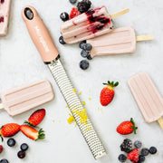 Microplane | Premium Zester, Grater - Dusty Rose with lemon zest, surrounded by berry-swirl ice pops and fresh berries on a countertop.