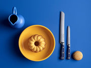 Wüsthof Classic 5 Serrated Utility Knife Wild Blueberry beside a small bundt cake on a plate, with a blue pitcher in the background.