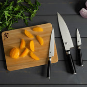 Shun | Classic Starter Set Ebony, 3 Pc displayed with peeled oranges and leafy greens on a cutting board, showcasing the versatile knives for essential kitchen tasks.