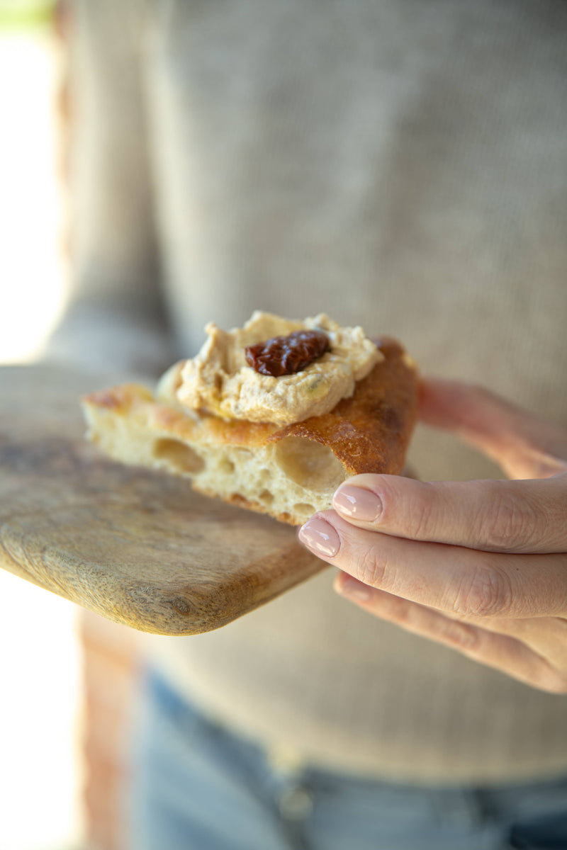 Person holding focaccia with TartufLanghe - Italian Parmigiano Truffle Cream topped with sun-dried tomato, showcasing gourmet potential of this luxurious spread from Athens Cooks.