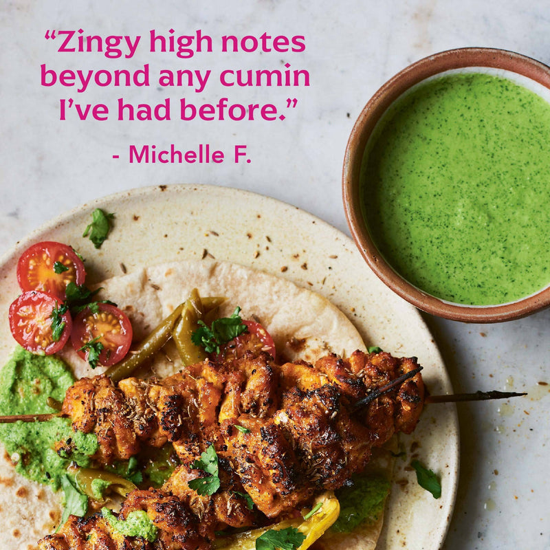 Skewered grilled chicken with herb sauce on flatbread, highlighting Diaspora Spices Co. - Jodhana Cumin's unique flavor. Accompanied by tomatoes, peppers, and extra sauce.