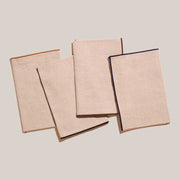 ATELIER SAUCIER - Dune Napkins | Set of 4: Natural linen napkins with bold, color-trimmed edges, neatly stacked, embodying understated elegance for a chic dining experience.