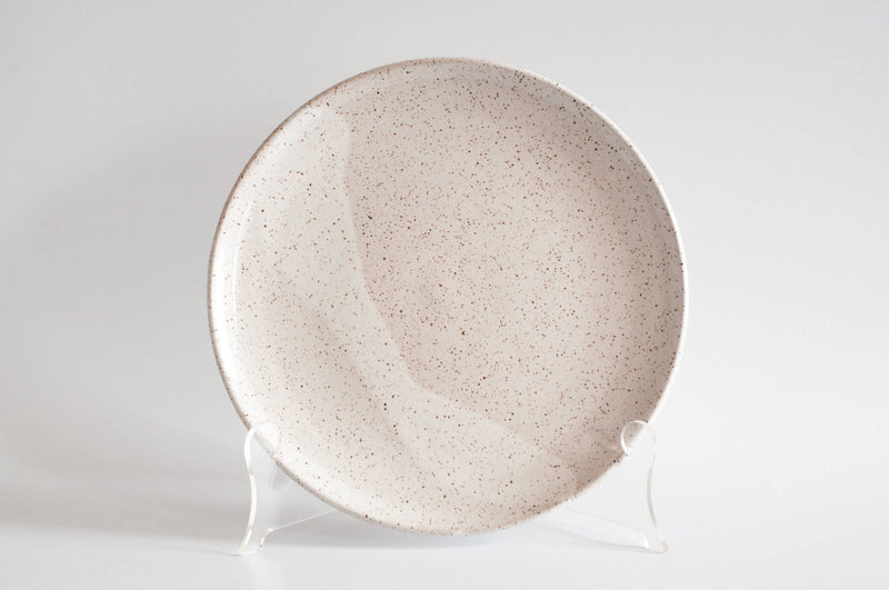 RachaelPots - Dinner Plate: Yellow, speckled off-white ceramic with a slightly upturned lip, displayed on a stand, highlighting handcrafted details.