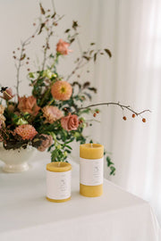 Mo&Co Home - 100% Beeswax Pillar Candles | Natural Gold: Two natural beeswax candles on a table, ideal for home decor and celebrations.