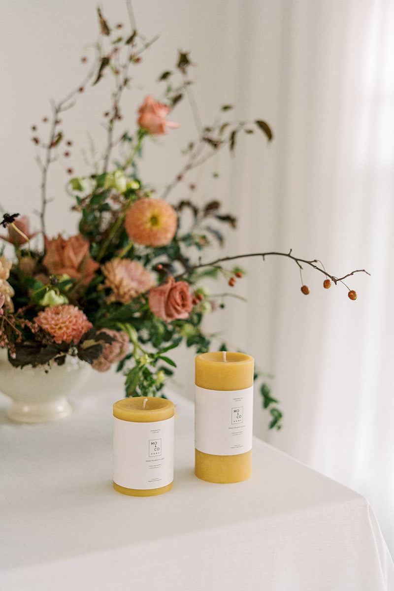 Mo&Co Home - 100% Beeswax Pillar Candles | Natural Gold: Two natural beeswax candles on a table, ideal for home decor and celebrations.