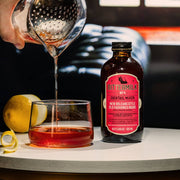 Bittermilk Bottling Co. - Bittermilk No.4 - New Orleans Style Old Fashioned Rouge being poured into a glass from a red-labeled bottle, showcasing its rich, bittersweet cocktail mix.
