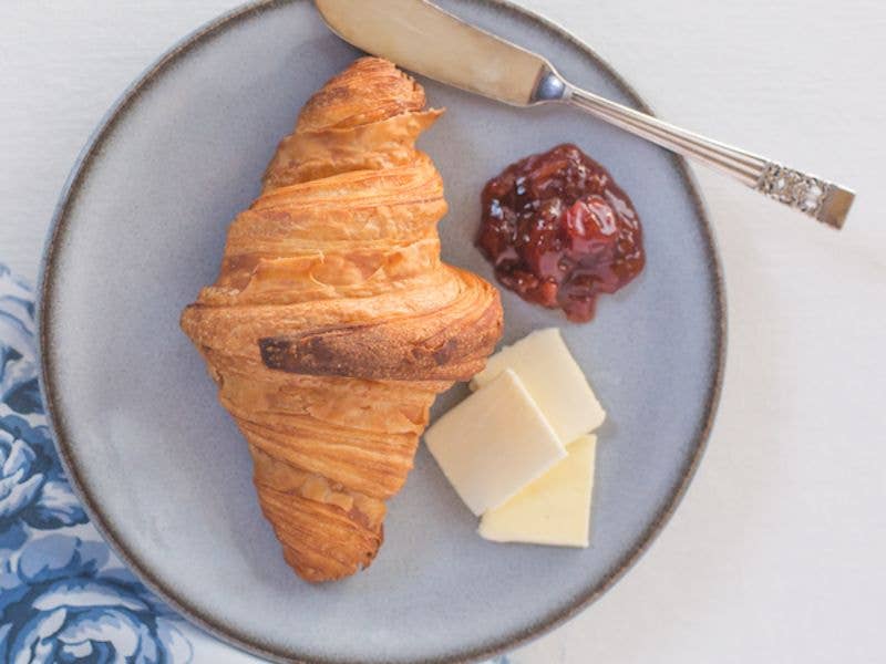 Beth's Farm Kitchen's Strawberry Rhubarb Jam pictured with a croissant, cheese slices, and a butter knife, showcasing a delectable breakfast setting.