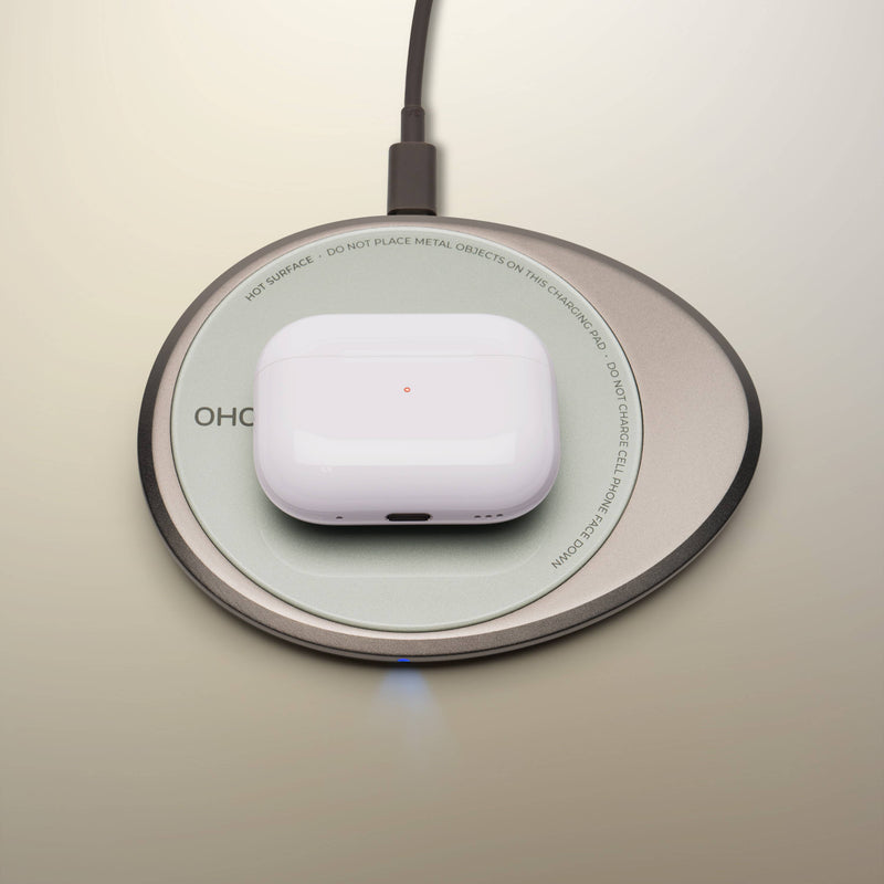 Wireless charging pad with a white earbuds case on top, part of the OHOM - Ui 3 Self-heating Mug Set, offering device charging and beverage warming.