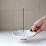 Gravesco Pottery - Incense Burner: A white-glazed ceramic dish with a central cone holding a black incense stick, designed for ash collection and tabletop protection.