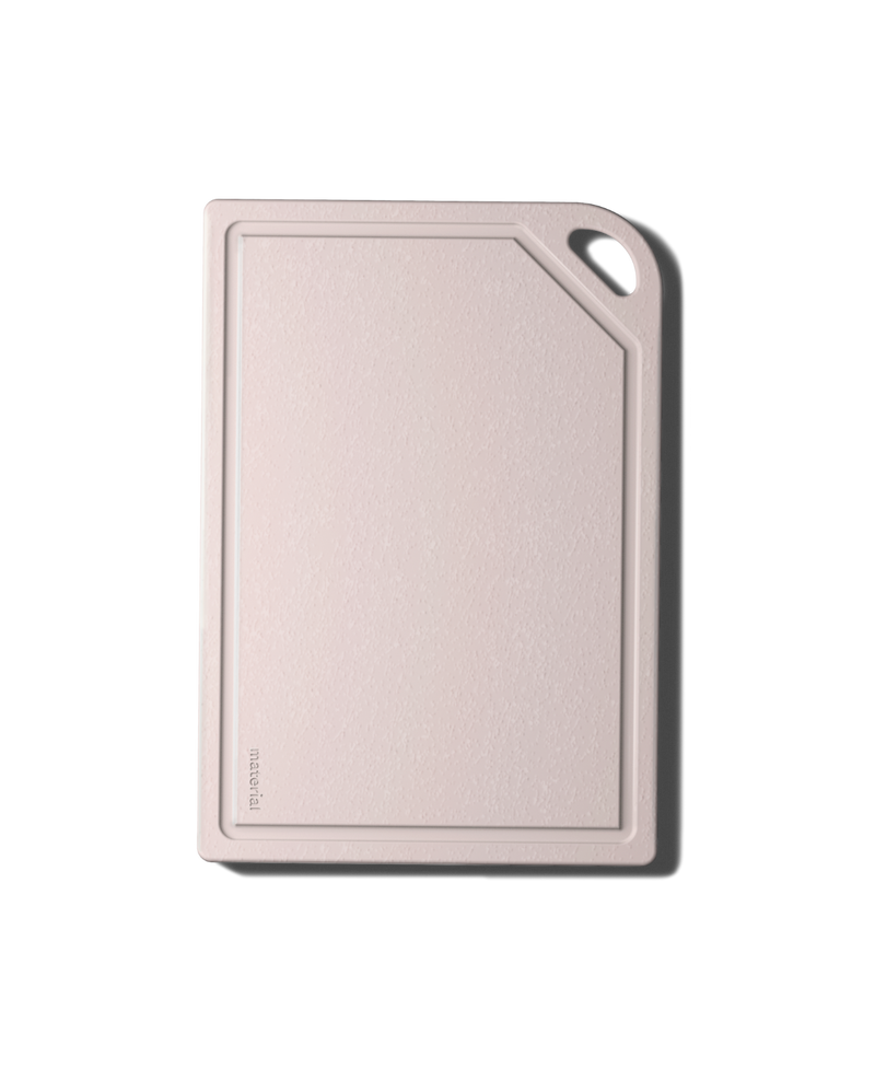 The MK Free Board: Ocean features a blush plant-based cutting board with a juice groove, embossed brand, and handle, ideal for safe, eco-friendly chopping.