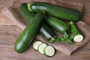 Bentley Seed Co. - Zucchini-Black Beauty Squash 1957 seeds displayed with fresh zucchinis on burlap, featuring whole, sliced pieces, and basil, ideal for diverse culinary uses.