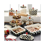 MacKenzie-Childs | Courtly Check Butter Box, a decorative black-and-white checkerboard ceramic butter dish with red finial, displayed among matching bakeware and storage items in a kitchen scene.