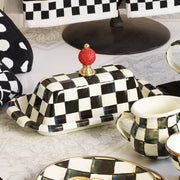 MacKenzie-Childs | Courtly Check Butter Box: A black-and-white checkerboard ceramic butter dish with a red knob, accompanied by a matching pitcher and plate.