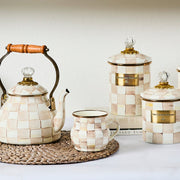 MacKenzie Childs | Mocha Check Mug showcased on a woven placemat, featuring hand-painted checks and bronzed stainless steel rim, with matching ceramic tea set and canisters.