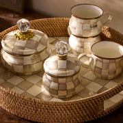 Round rattan tray with MacKenzie Childs' Mocha Check Lidded Sugar Bowl, featuring hand-painted checks and glass knob, accompanied by matching ceramic mugs.