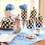 MacKenzie Childs Courtly Check Medium Canister on a table with tea and cookies, showcasing its hand-painted design and versatile kitchen storage use.