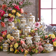 Sterling Check Medium Canister by MacKenzie-Childs amidst vibrant spring blooms, featuring hand-painted checks, gilded accents, and a crystal-style knob, perfect for kitchen storage.