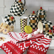 MacKenzie-Childs Cookie Jar with Courtly Check Lid sits among checkerboard kitchenware and cookies, showcasing its glass body and hand-painted lid, embodying stylish kitchen functionality.