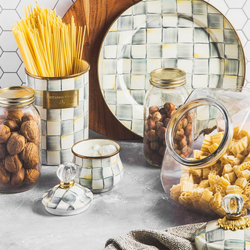 MacKenzie Childs | Cookie Jar with Sterling Check Lid on a styled kitchen counter, surrounded by decorative canisters, glass jars with nuts, and spilling pasta.