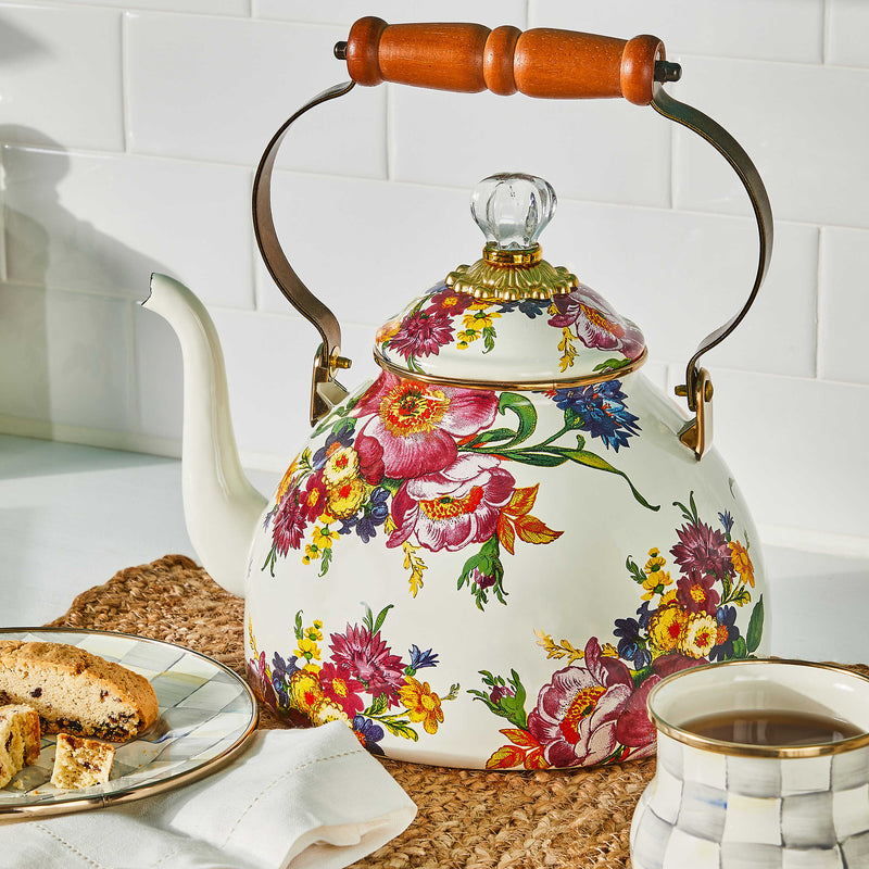 MacKenzie-Childs White Flower Market Tea Kettle with floral design, wooden handle, sits on placemat beside biscotti and matching mug in an Athens Cooks kitchen setting.