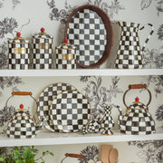 MacKenzie Childs | Courtly Check Tea Kettle, 3 QT., featuring hand-painted checks, wood handle, and brass-accented lid, displayed on a shelf with matching kitchenware.