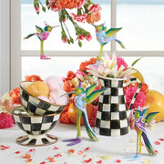 MacKenzie-Childs Courtly Check Ice Cream Dish with ice cream, surrounded by vibrant carnations and hummingbird figurines, showcasing elegant design and charm from Athens Cooks.