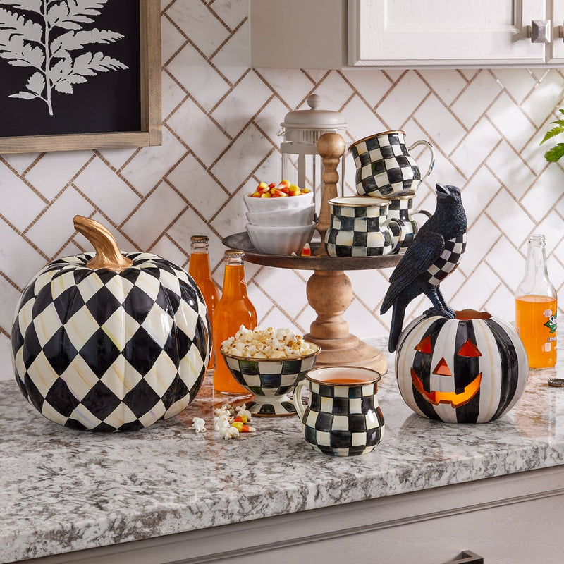 MacKenzie-Childs | Courtly Check Ice Cream Dish amidst a Halloween-themed kitchen setup, showcasing its black-and-white check pattern alongside decorative pumpkins and a two-tiered wooden stand.