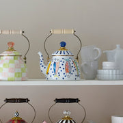 Mackenzie Childs | Go Fish Tea Kettle, 2 QT., displayed with cups and saucers on a two-tier shelf, showcasing intricate hand-painted details and craftsmanship.