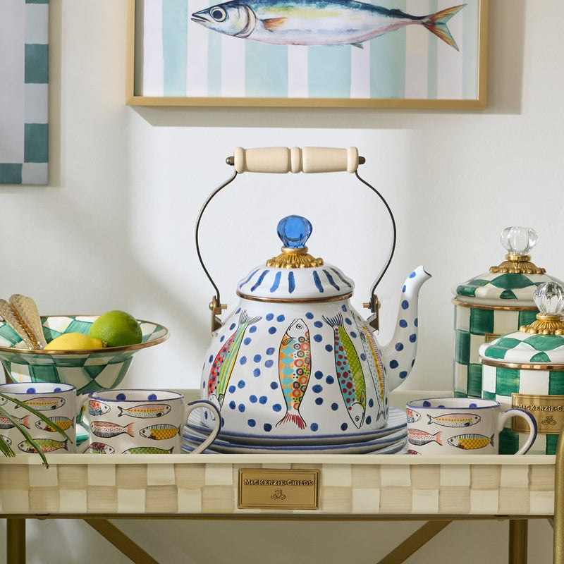 MacKenzie-Childs Go Fish Tea Kettle, 2 QT, with hand-painted fish design, wooden handle, and glass finial, amidst matching mugs and kitchen accessories on a tray.