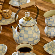 MacKenzie-Childs Sky Check Tea Kettle, 2 Qt, with blue-and-white checkerboard pattern, wooden handle, surrounded by matching mugs, plates, and blueberry muffins on a wooden table.