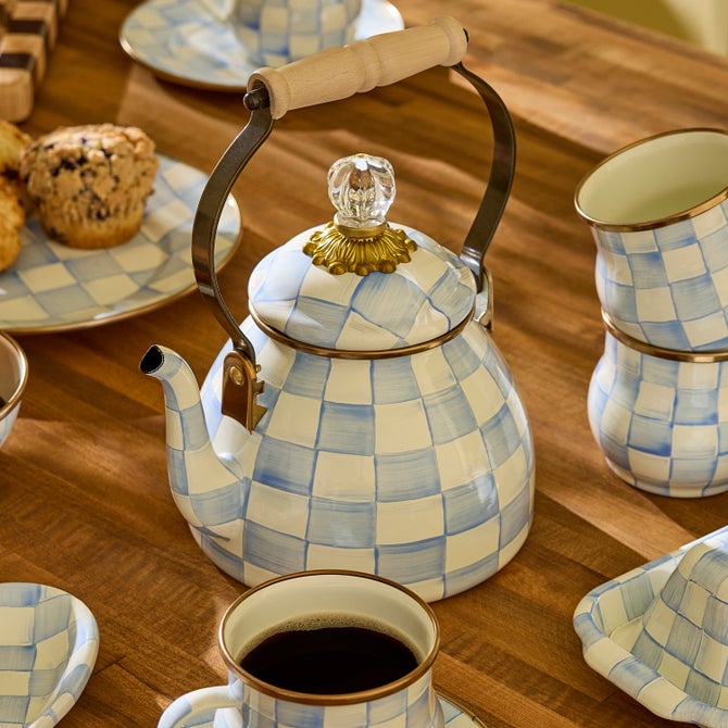 MacKenzie-Childs Sky Check Tea Kettle, 2 Qt, with blue-and-white checkerboard pattern, wooden handle, surrounded by matching mugs, plates, and blueberry muffins on a wooden table.