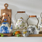 MacKenzie Childs | Wildflowers Pink Tea Kettle, 2 QT., with floral design, wooden handle, glass-topped lid, set among fruit and cutting boards in a cozy kitchen scene.