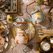 MacKenzie-Childs Wild Rose Mauve Tea Kettle, 2 Qt, with wooden handle and floral design, displayed on a tabletop with matching plates and vintage accents.