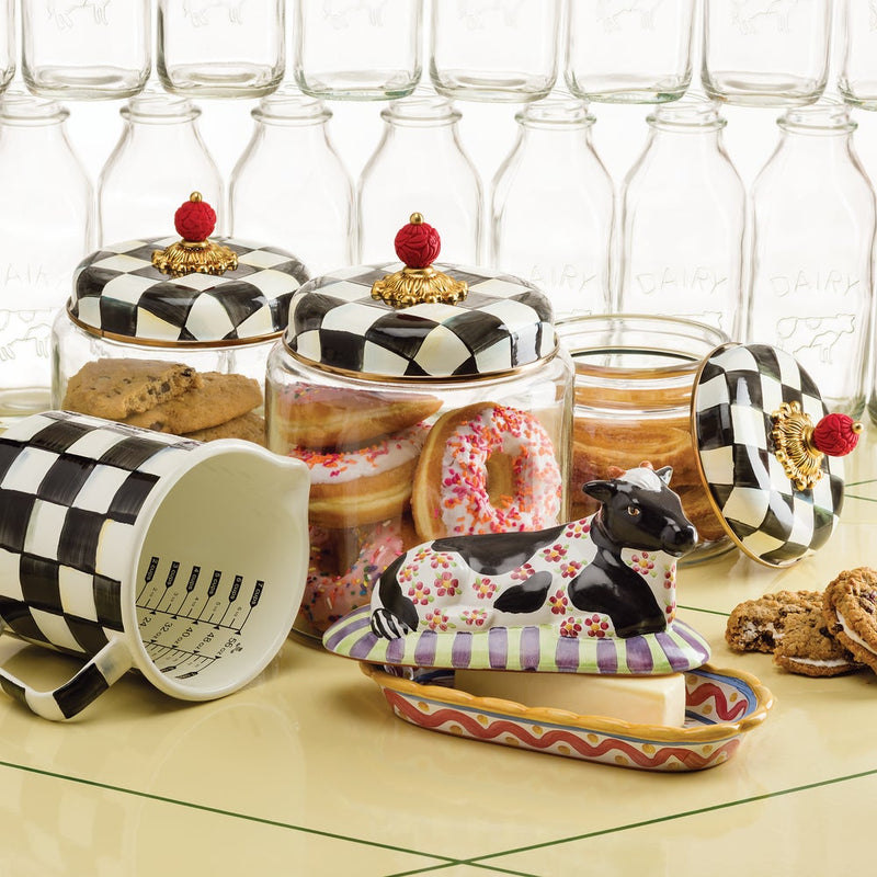 MacKenzie-Childs Courtly Check 7 Cup Measuring Cup showcased on a countertop with cookies, donuts, and a cow-shaped butter dish, highlighting its artistic, hand-glazed design.