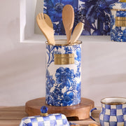 MacKenzie-Childs Royal English Garden Utensil Holder on wooden trivet, filled with wooden tools, beside matching butter dish and mug on a kitchen countertop.