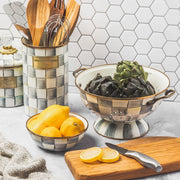 MacKenzie Childs Sterling Check Utensil Holder filled with wooden utensils on a styled kitchen countertop, featuring matching accessories with a hand-painted checkerboard pattern and artichokes.