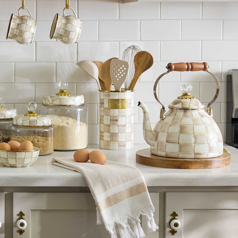 MacKenzie Childs | Mocha Check Utensil Holder displayed on a kitchen counter with nearby teapots and utensils, showcasing its hand-painted checks and bronzed stainless-steel rim.