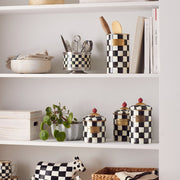 MacKenzie-Childs Courtly Check Utensil Holder on checkerboard shelving, filled with wooden spoons, alongside matching kitchen decor and storage canisters.