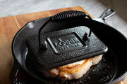 Lodge 8 Round Cast Iron Grill Press in a cast iron skillet, showcasing its seasoned surface ideal for pressing sandwiches or bacon, enhancing your culinary creations.