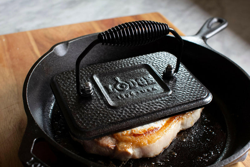 Lodge 8 Round Cast Iron Grill Press in a cast iron skillet, showcasing its seasoned surface ideal for pressing sandwiches or bacon, enhancing your culinary creations.