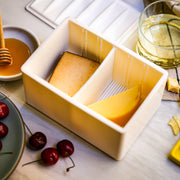 CapaBunga® Cheese Vault in white, showcasing two cheese varieties with cherries, honey, and a glass of wine, demonstrating stylish cheese storage from Athens Cooks.