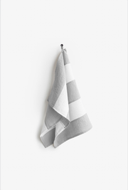 Striped linen tea towel hanging on a hook, showcasing its loop for easy storage. Made from natural linen in a zero-waste initiative.