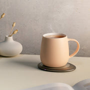 OHOM - Ui 3 Self-heating Mug Set: Jasmine White on warming coaster, steaming drink inside; nearby, a vase with dried flowers and an open book.