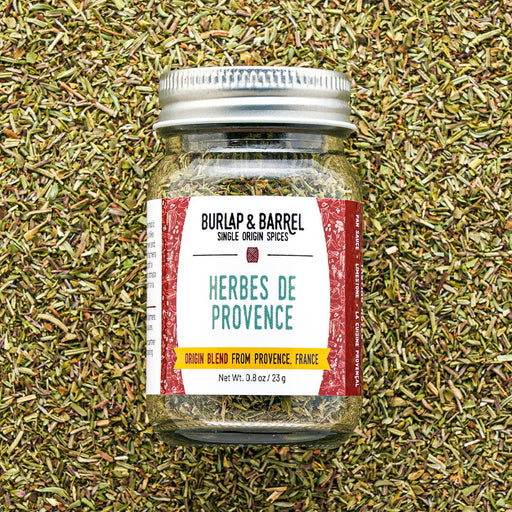 Burlap & Barrel - Herbes de Provence - Single Origin Spice & Seasoning Blend: 0.8 oz glass jar with metal lid, set against a backdrop of loose herbs.
