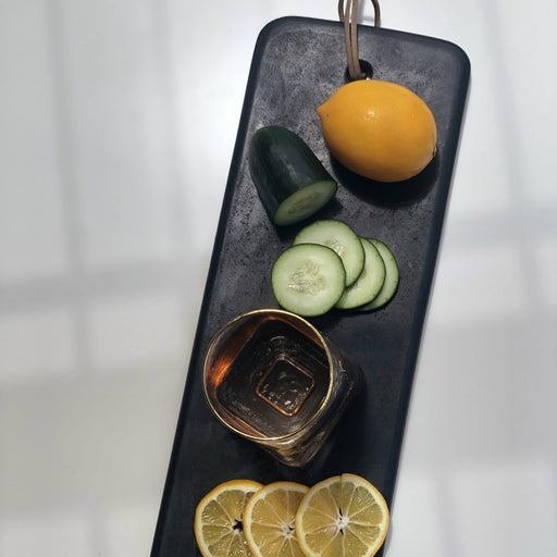 Couleur Nature - Pepe Marble Cheese Board, Large Black, showcasing a whole lemon, cucumber slices, lemon slices, and a gold-toned cup, ideal for elegant cheese arrangements.