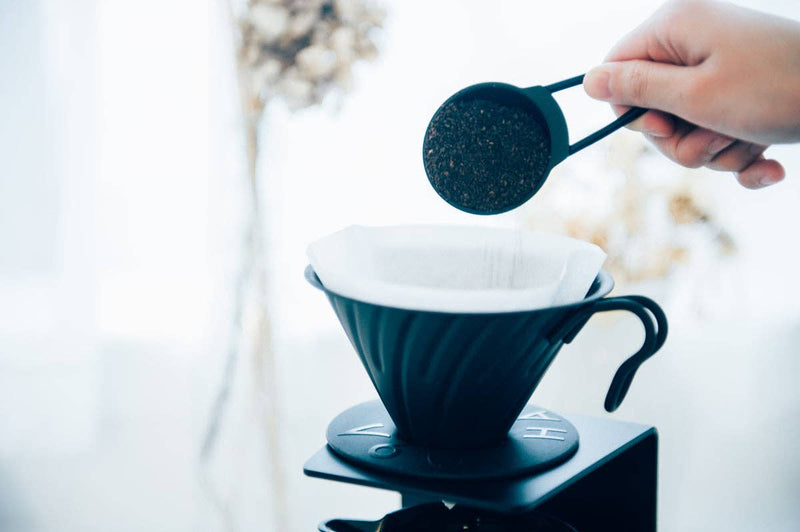 HARIO USA - V60 Metal Dripper: Silver in use, ground coffee being measured over the dripper on a scale, ready for brewing.