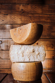 Nicola's Marketplace - Parmigiano Reggiano DOP Mitica® 36 months: 7 Ounces. Stacked aged cheese wheels, revealing crumbly interior and stamped rind, showcasing artisanal quality.