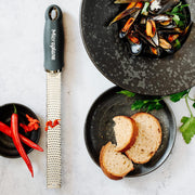 Microplane | Premium Zester, Grater - After Dark Grey, on countertop with chili, mussels, and bread, showcasing ergonomic handle and stainless-steel blade.