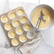 Nordic Ware Large Cookie Dropper shown beside a bowl of batter and a tray of cupcakes, ideal for precision baking.