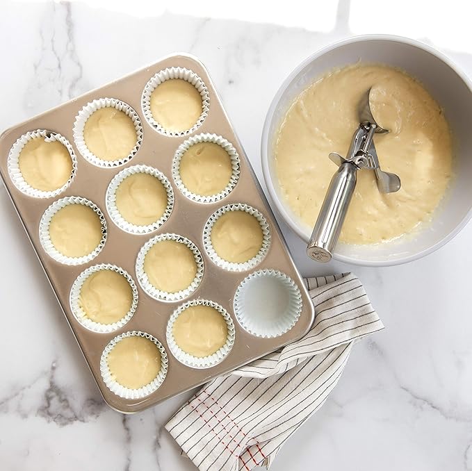 Nordic Ware Large Cookie Dropper shown beside a bowl of batter and a tray of cupcakes, ideal for precision baking.